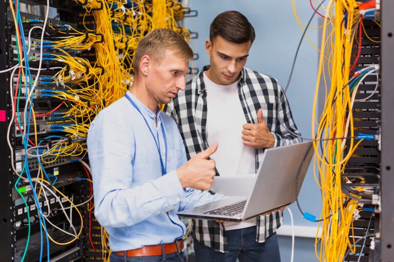 two men looking at a laptop in a server room